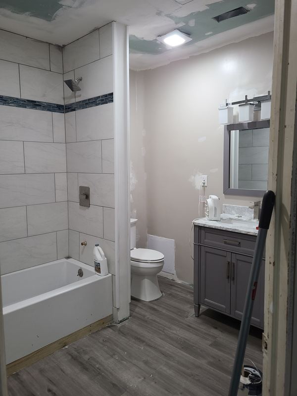 Renovated bathroom with tub surround, vanity, and plank flooring
