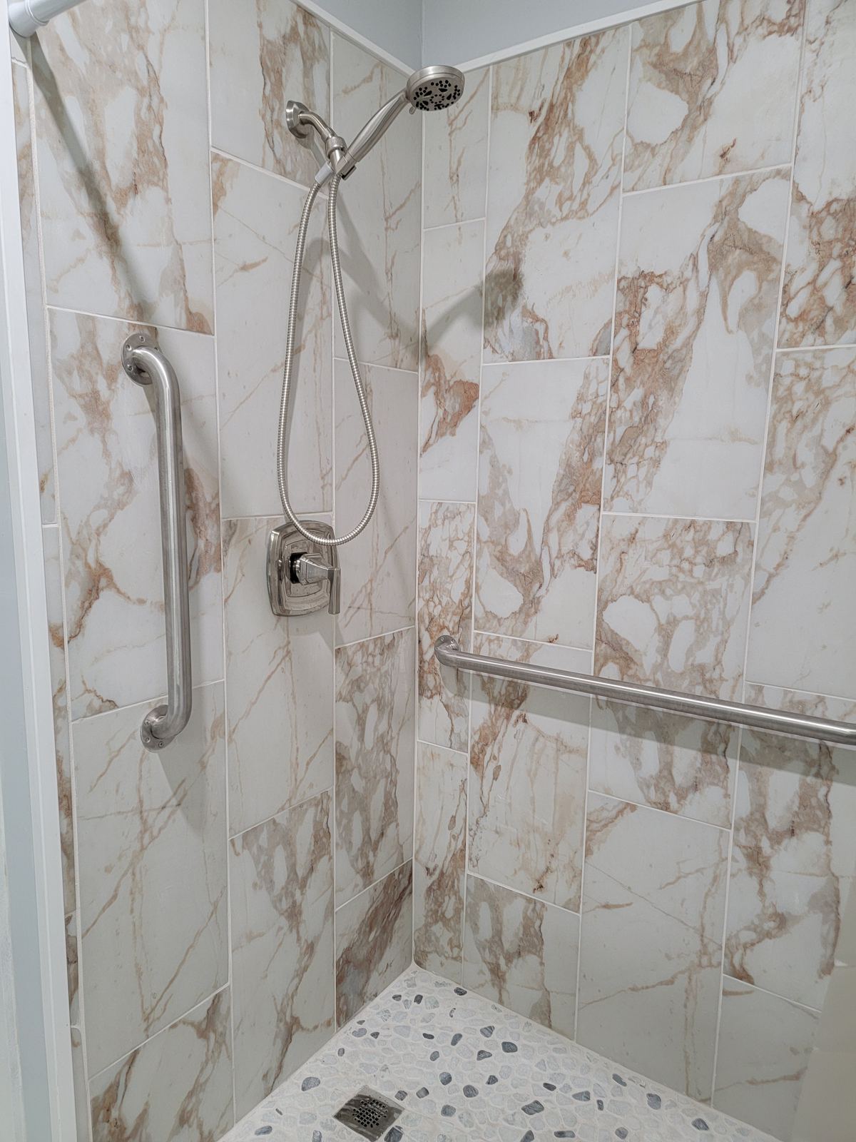 Marble-look tiled shower with wall-mounted grab bars and a handheld shower